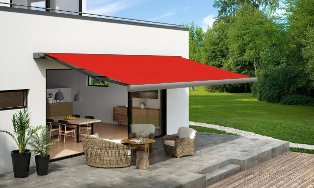 Toldo rojo extendido sobre un patio con muebles de mimbre, ofreciendo ideas para dar sombra en un patio.