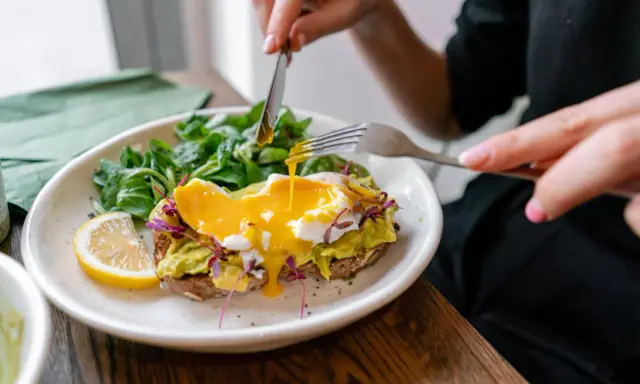 Tost z awokado i jajkiem sadzonym, polany żółtkiem, z sałatką i cytryną.