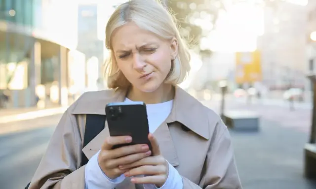 Zmarszczona kobieta patrzy na telefon, zastanawiając się, jak przestać zazdrościć innym.