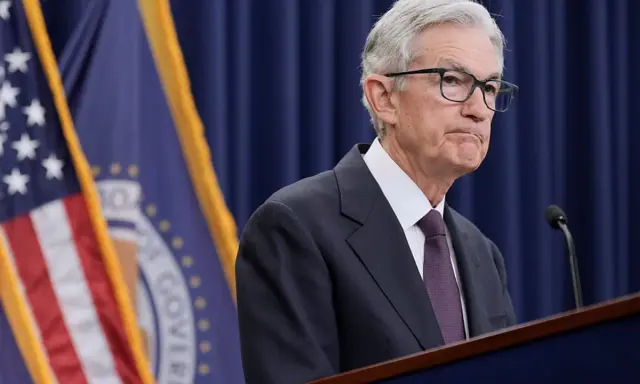 Jerome Powell przemawia na tle flag USA i Rezerwy Federalnej, instytucji, która budzi pytania, czy fed jest prywatny.