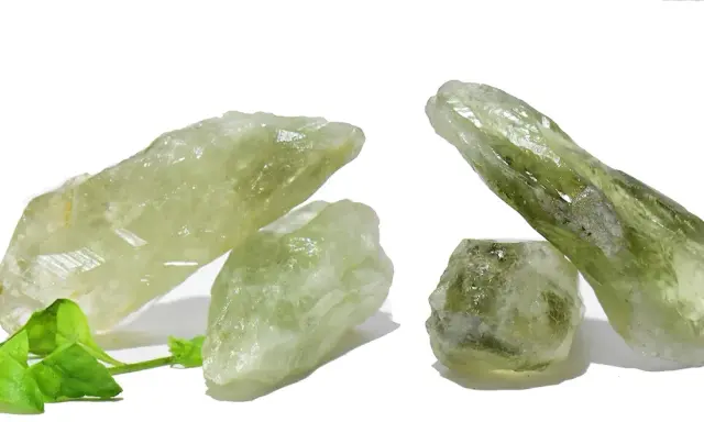 Cristalli grezzi di ametista verde, noti per il loro significato di crescita e rinnovamento, su sfondo bianco con foglie verdi.