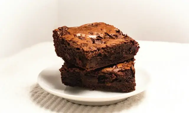 Dwa wilgotne ciasta brownie z płynną czekoladą, ułożone jedno na drugim na białym talerzyku.