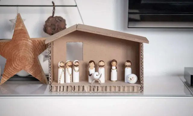 Eine einfache Krippe basteln Kinder mit Holzfiguren und Karton. Maria, Josef und das Jesuskind sind in der Mitte, umgeben von Hirten und einem Schaf.