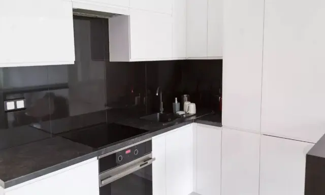 Nowoczesna, biała kuchnia z eleganckim, ciemnym blatem. Czarna płyta indukcyjna i zlew tworzą spójną całość.