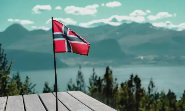 Norweska flaga na tle gór i jeziora. Pomyśl o tym, jak wysłać zwolnienie lekarskie do NAV, gdy jesteś w tak pięknych okolicznościach.