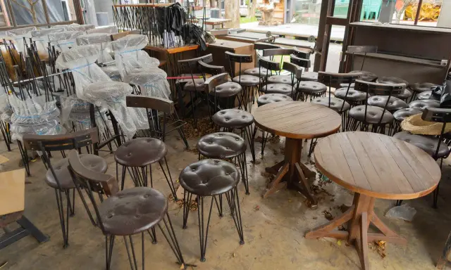 Viele gebrauchte Gastrostühle und runde Holztische stehen in einem Raum.