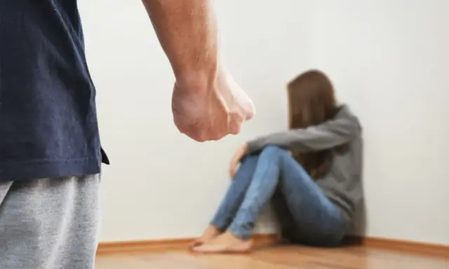 Zaciśnięta pięść mężczyzny grozi skulonej kobiecie. Scena symbolizuje agresję żony wobec męża, przemoc domową.