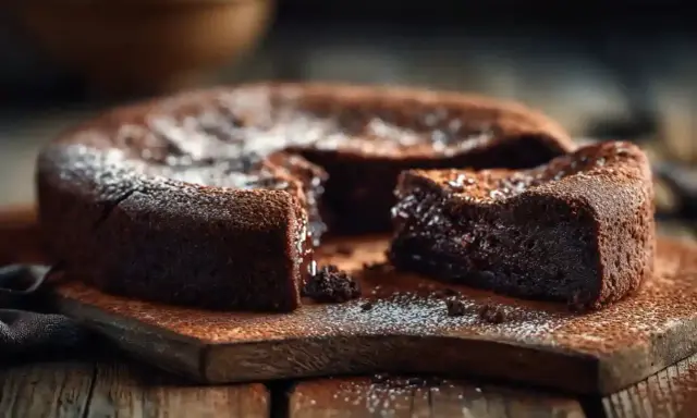 Un délicieux cake au chocolat, saupoudré de sucre glace, est servi sur une planche en bois rustique. Une part est coupée, révélant sa texture moelleuse.