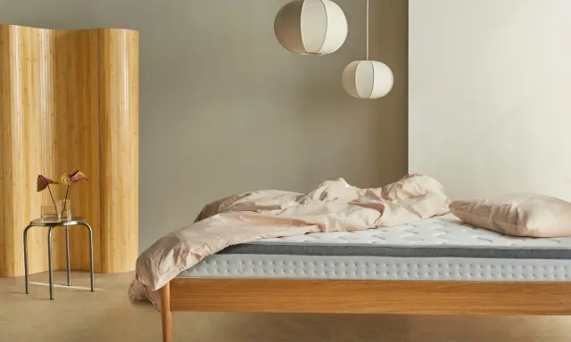 Una habitación nórdica con cama de madera, ropa de cama rosa y un biombo de bambú.