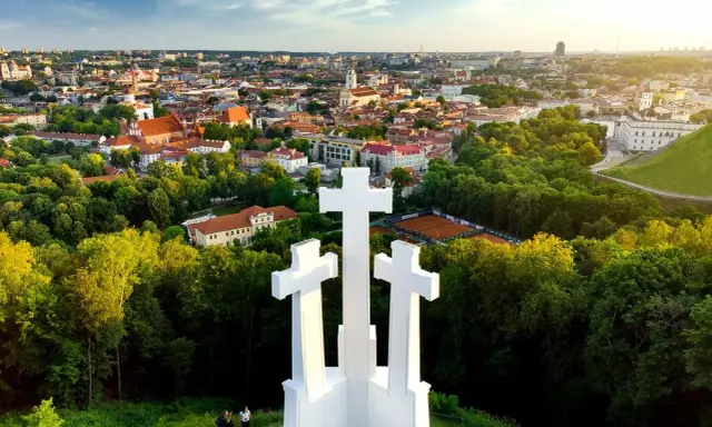 Wzgórze Trzech Krzyży w Wilnie z widokiem na miasto. Trzy białe krzyże górują nad zielonymi drzewami i zabytkową architekturą.
