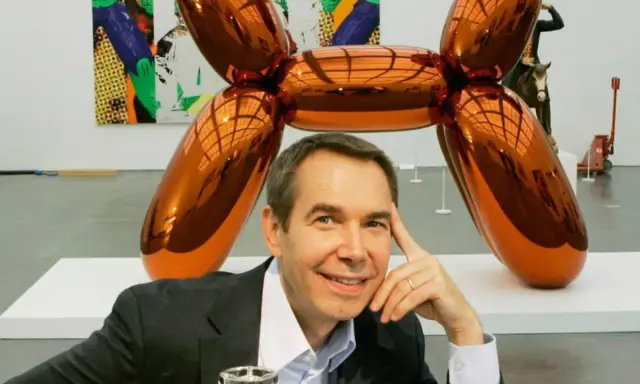 Jeff Koons posa junto a su icónica escultura perro globo naranja brillante en una galería de arte.