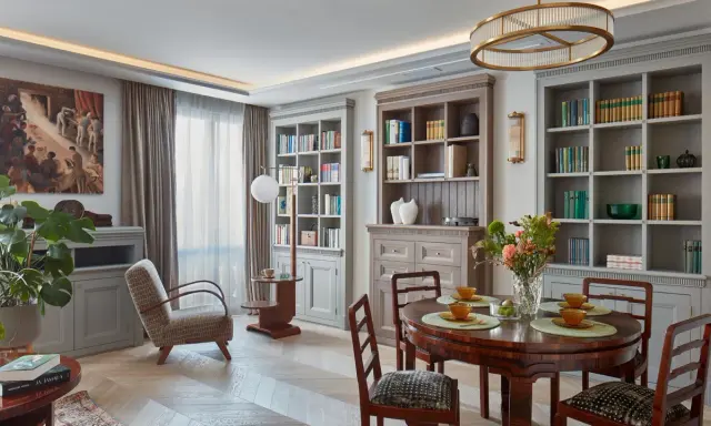 Elegancki salon w stylu art deco z dwoma regałami pełnymi książek, okrągłym stołem i wygodnym fotelem.