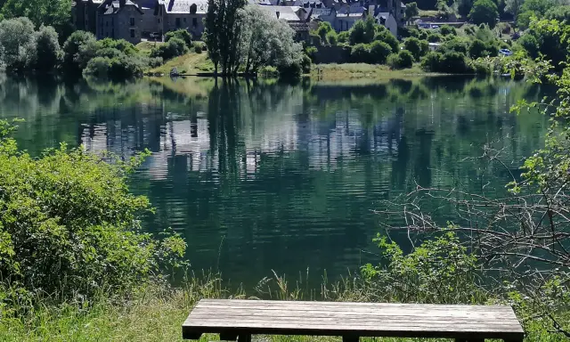 Un banco de madera invita a contemplar el embalse de Lanuza, con un pueblo de tejados grises reflejado en sus tranquilas aguas verdes.