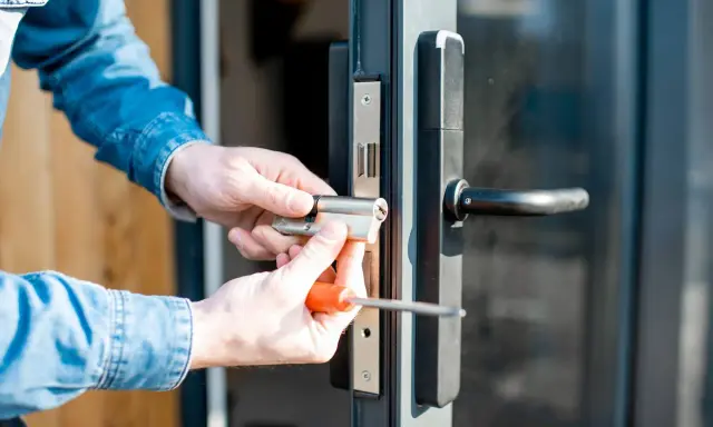 Man con camisa de mezclilla instala un cilindro de cerradura en una puerta, resolviendo un problema de comodato precario.