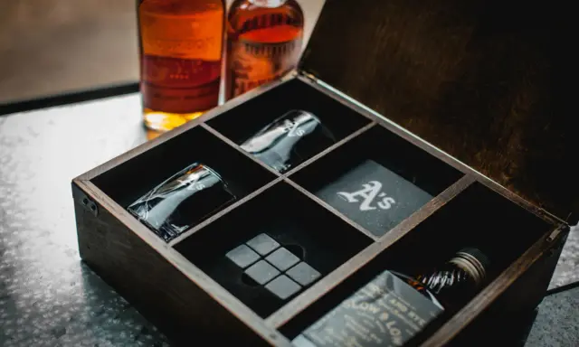 Elegancki zestaw z whisky w drewnianej skrzynce: dwie butelki, kieliszki z monogramem "A's", kamienie do whisky i podkładka.
