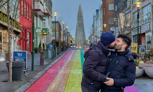 A couple shares a kiss on a rainbow-painted street in gay Reykjavik, with Hallgrímskirkja church in the background.