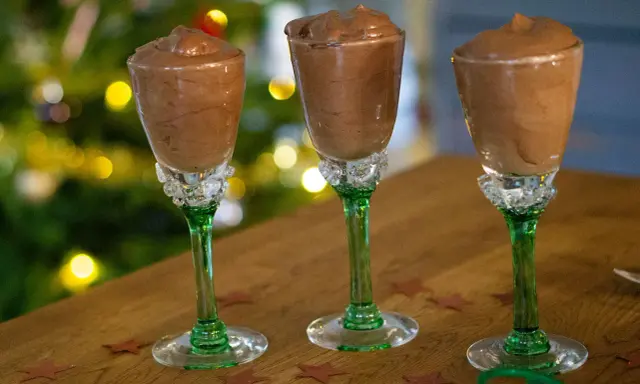 Tre glas med krämig chokladmousse, perfekta för ett enkelt chokladmousse recept. Julbelysning i bakgrunden skapar en festlig stämning.