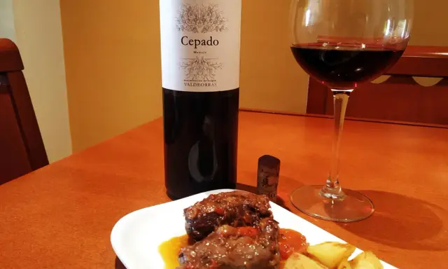 Un plato de carrilleras estofadas con patatas, acompañado de una copa de vino tinto Cepado Mencía, ideal para maridar.
