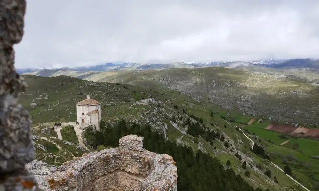 Un piccolo santuario domina il paesaggio del **cammino del Gran Sasso**, tra colline verdi e montagne nebbiose.