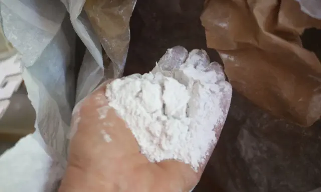 Main d'une personne tenant une poudre blanche fine, de la chaux morte, sortant d'un sac en papier.