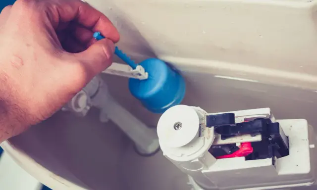 Main tenant répare chasse d'eau bouton poussoir. Il ajuste le flotteur bleu pour un bon fonctionnement.