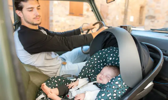 Padre atento conduce mientras su bebé duerme plácidamente en su silla de auto, listo para viajar con bebes.