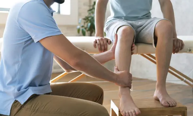 Un podologue examine la jambe d'un patient, un examen essentiel pour la podologie.