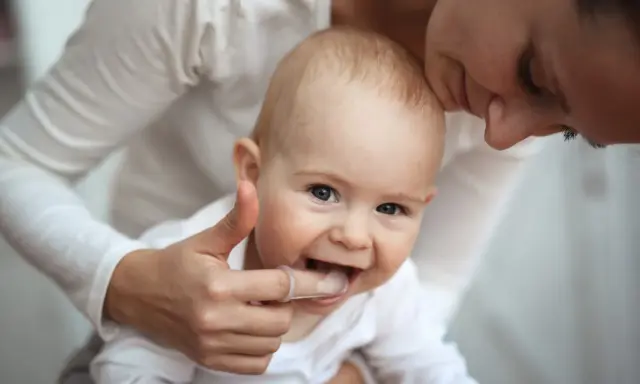 Mama pomaga dziecku z kolejnością wychodzenia zębów, delikatnie masując dziąsła palcem w nakładce.