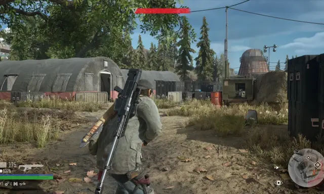 Gracz w Days Gone Remastered z karabinem na plecach przemierza obóz z namiotami i kontenerami.