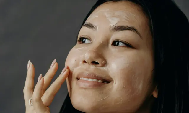Donna applica una crema sul viso, un gesto quotidiano per come curare la pelle del viso.