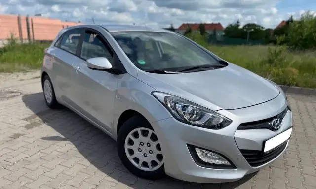 Srebrny Hyundai i30 1.4 benzyna zaparkowany na kostce brukowej, w tle zielona trawa i budynki.