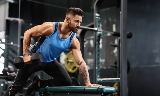 Mann mit Bart macht einbeiniges Rudern mit Kurzhantel. Fokus auf Muskelaufbau Training im Fitnessstudio.