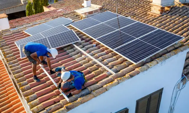 Dos técnicos instalan placas solares en un tejado. Aprendiendo como instalar placas solares para un futuro energético.