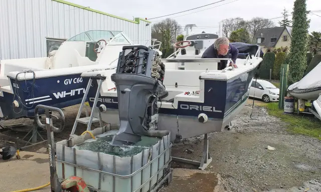 Un homme effectue le rinçage moteur hors bord vinaigre blanc d'un bateau. L'hélice est immergée dans une cuve remplie de liquide.