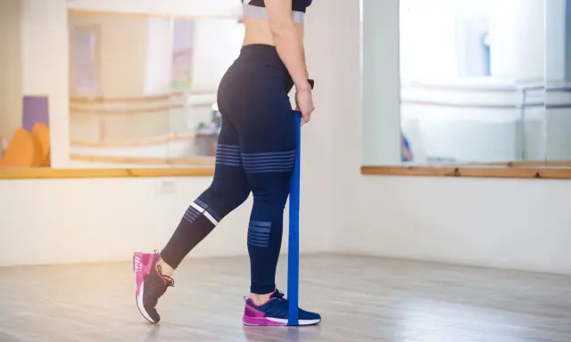 Frau trainiert Beine mit Widerstandsband. Sanftes, gelenkschonendes **low impact training** für Kraft und Ausdauer.