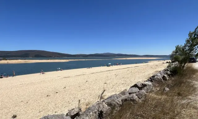 Gente disfrutando del sol y el agua en la playa de Arija, con montañas al fondo y un cielo azul despejado.