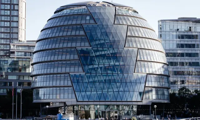 Edificio iconico di Norman Foster, con facciata a diamante in vetro, riflette il cielo e gli edifici circostanti.