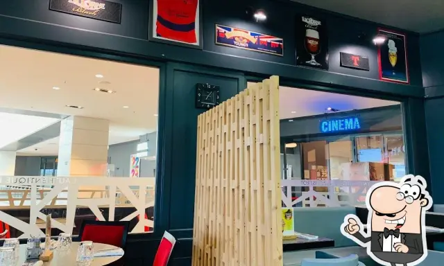 Ambiance chaleureuse à la trattoria Ibos, avec des décorations de rugby et de bière. Une enseigne "CINEMA" brille au loin.