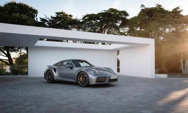 Silberner Porsche Turbo S, bereit für den 0-100 Sprint, parkt vor moderner Architektur im Sonnenuntergang.