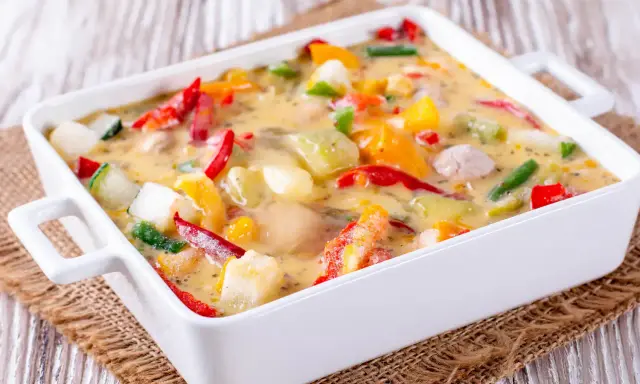 Un gratin de légumes coloré et crémeux, avec des poivrons, courgettes et autres légumes dans une sauce onctueuse, prêt à être dégusté.