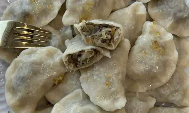 Pyszne pierogi z kapustą i pieczarkami, jeden przekrojony, by pokazać bogate nadzienie. Złoty widelec obok.