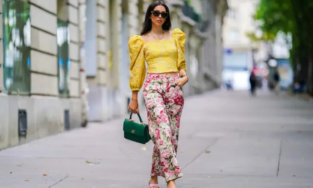 A woman shows that a woman can wear pants for cocktail attire, sporting a yellow puff-sleeve top and floral pants.