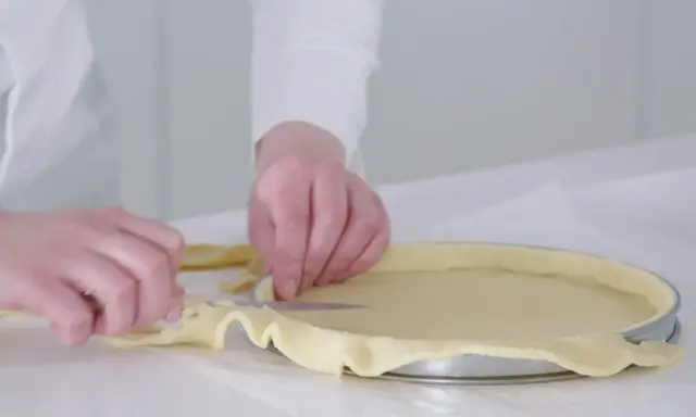 Préparation de la pâte pour une recette biscuit noisette. Les mains ajustent la pâte dans un moule à tarte.