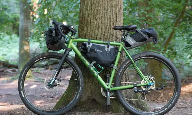 Grünes Gravelbike mit Taschen für Bike Packing, bereit für Abenteuer im Wald.