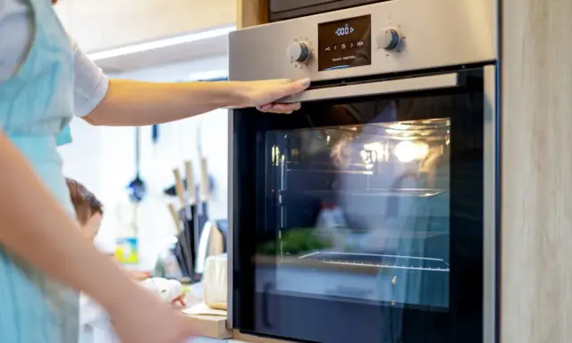 Une main ajuste la porte d'un four encastrable. La lumière intérieure est allumée, prêt pour la cuisson.