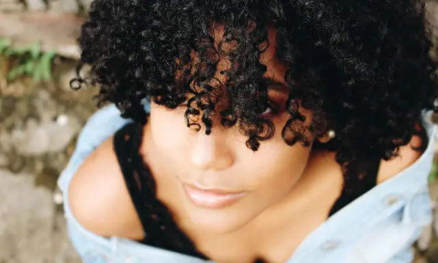 Une jeune femme aux cheveux bouclés naturels, une coiffure cheveux bouclés facile et magnifique, porte une veste en jean.