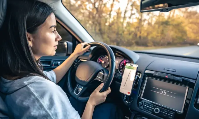 Kobieta prowadzi auto, a telefon z nawigacją zamontowany jest na desce rozdzielczej. Idealne miejsce, gdzie zamontować uchwyt na telefon w samochodzie.