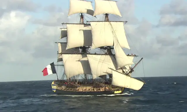 La frégate Hermione, fierté de la marine française, navigue majestueusement sur l'océan, ses voiles gonflées par le vent.