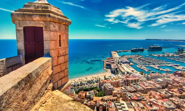 Alicante co zobaczyć: widok z zamku na port, plażę i miasto. W oddali statki wycieczkowe.