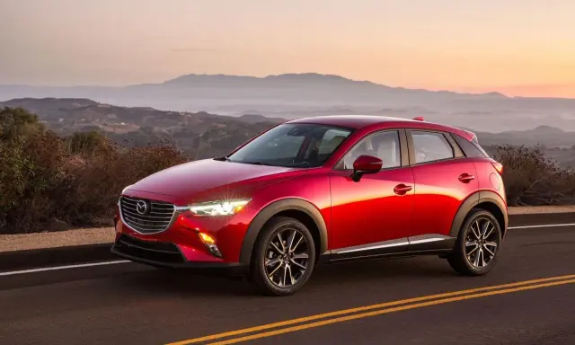Czerwona Mazda CX-3 na tle górskiego krajobrazu o zachodzie słońca. Elegancka linia nadwozia i lśniący lakier.